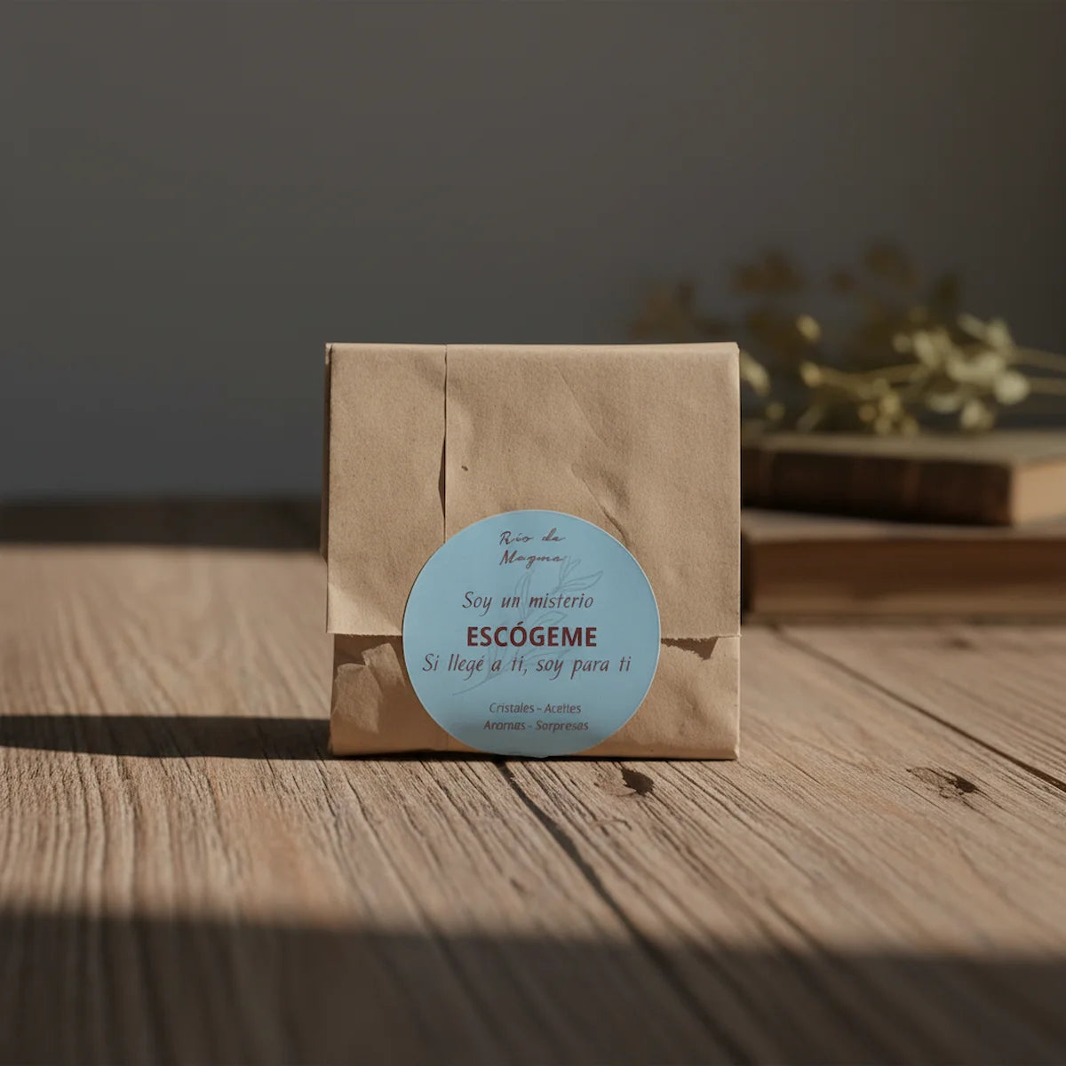 Paquete kraft cerrado de Colección Misterio con sticker celeste, sobre superficie de madera con luz lateral