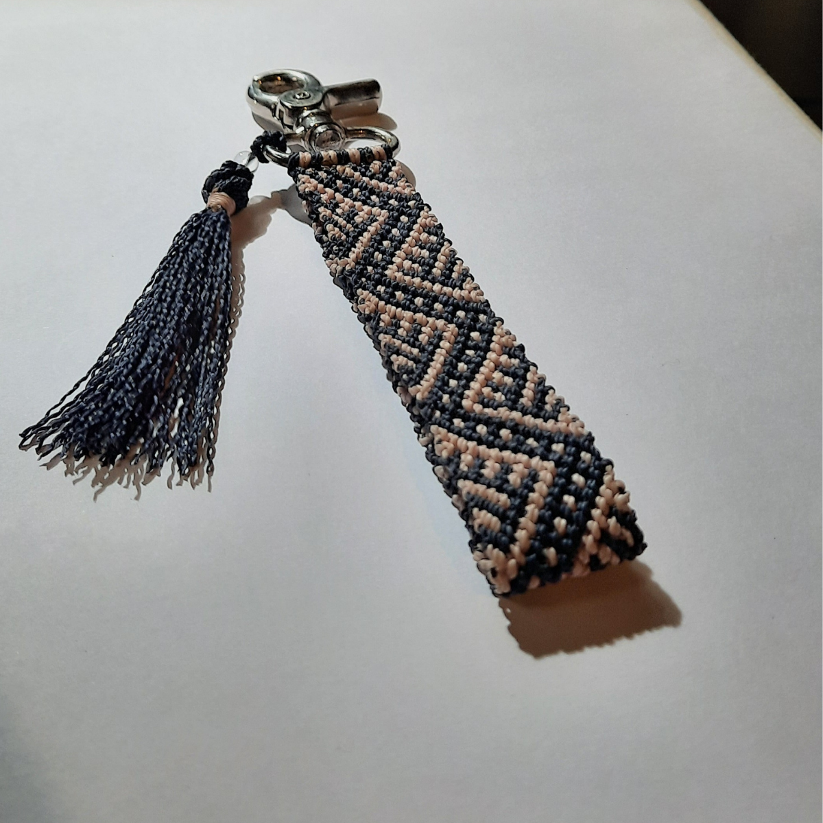 Detalle de llavero artesanal de macramé con mosquetón metálico y borla decorativa tejida.