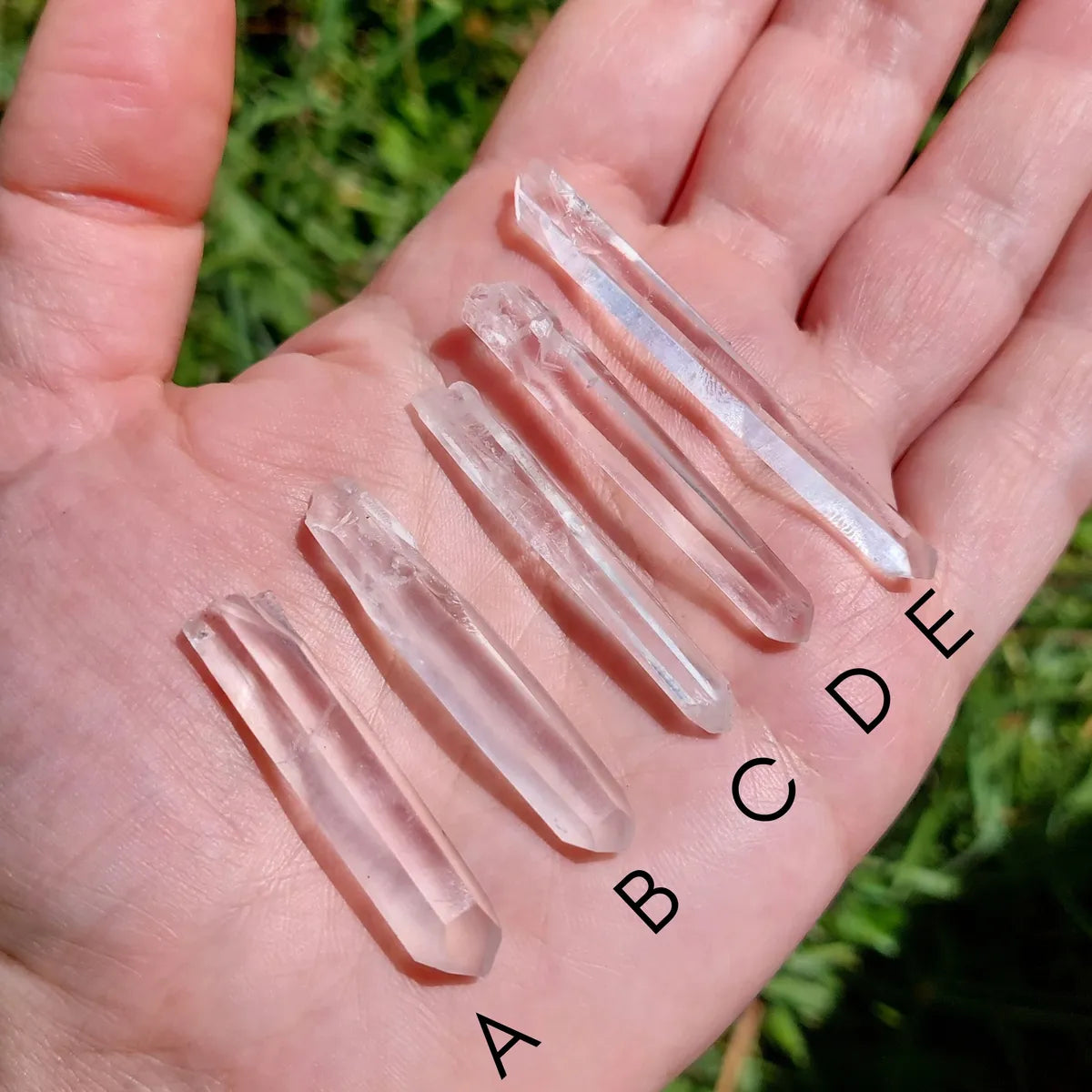Puntas naturales de cuarzo traslúcido sobre la mano con variantes de la A a la J.