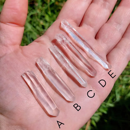 Puntas naturales de cuarzo traslúcido sobre la mano con variantes de la A a la J.