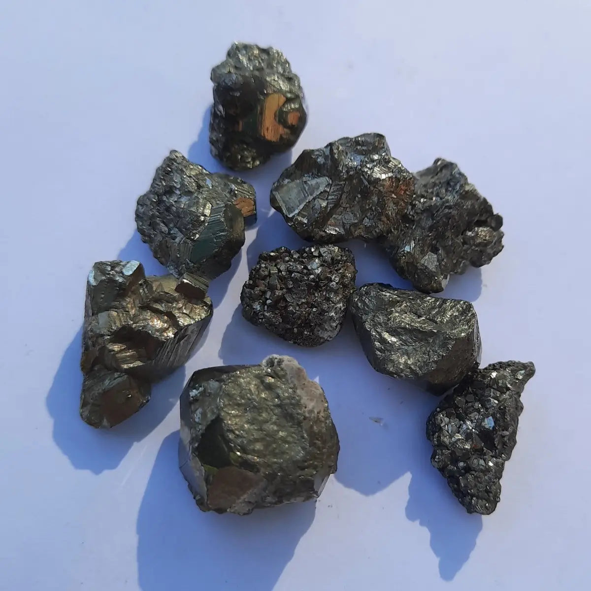 Piezas de pirita natural en bruto de pequeño tamaño, con brillo metálico dorado sobre fondo blanco y luz natural