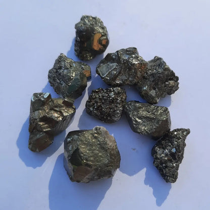 Piezas de pirita natural en bruto de pequeño tamaño, con brillo metálico dorado sobre fondo blanco y luz natural