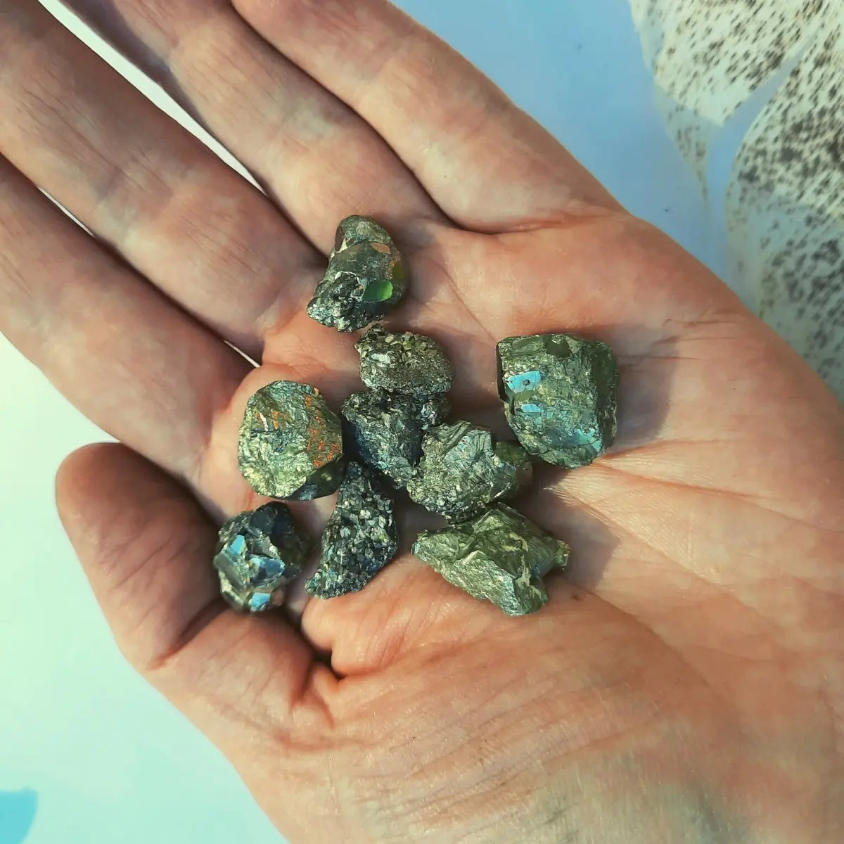 Piezas de pirita natural en bruto de pequeño tamaño, con brillo metálico dorado sobre mano indicando tamaño y forma.