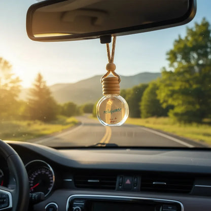 Frasco esférico de vidrio con tapa de madera y cordón colgando del espejo retrovisor, con texto "relajante · Río de Magma", carretera y árboles al fondo con luz de atardecer
