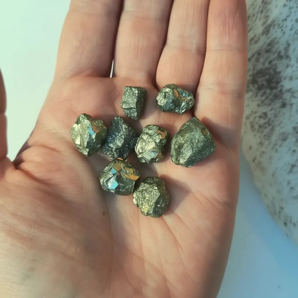 Piezas de pirita natural en bruto de pequeño tamaño, con brillo metálico dorado sobre mano indicando tamaño y forma.