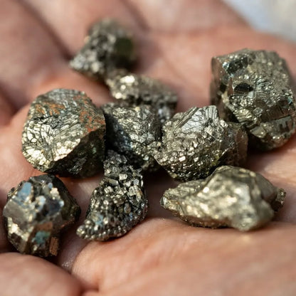 Piezas de pirita natural en bruto de pequeño tamaño, con brillo metálico dorado sobre mano indicando tamaño y forma.