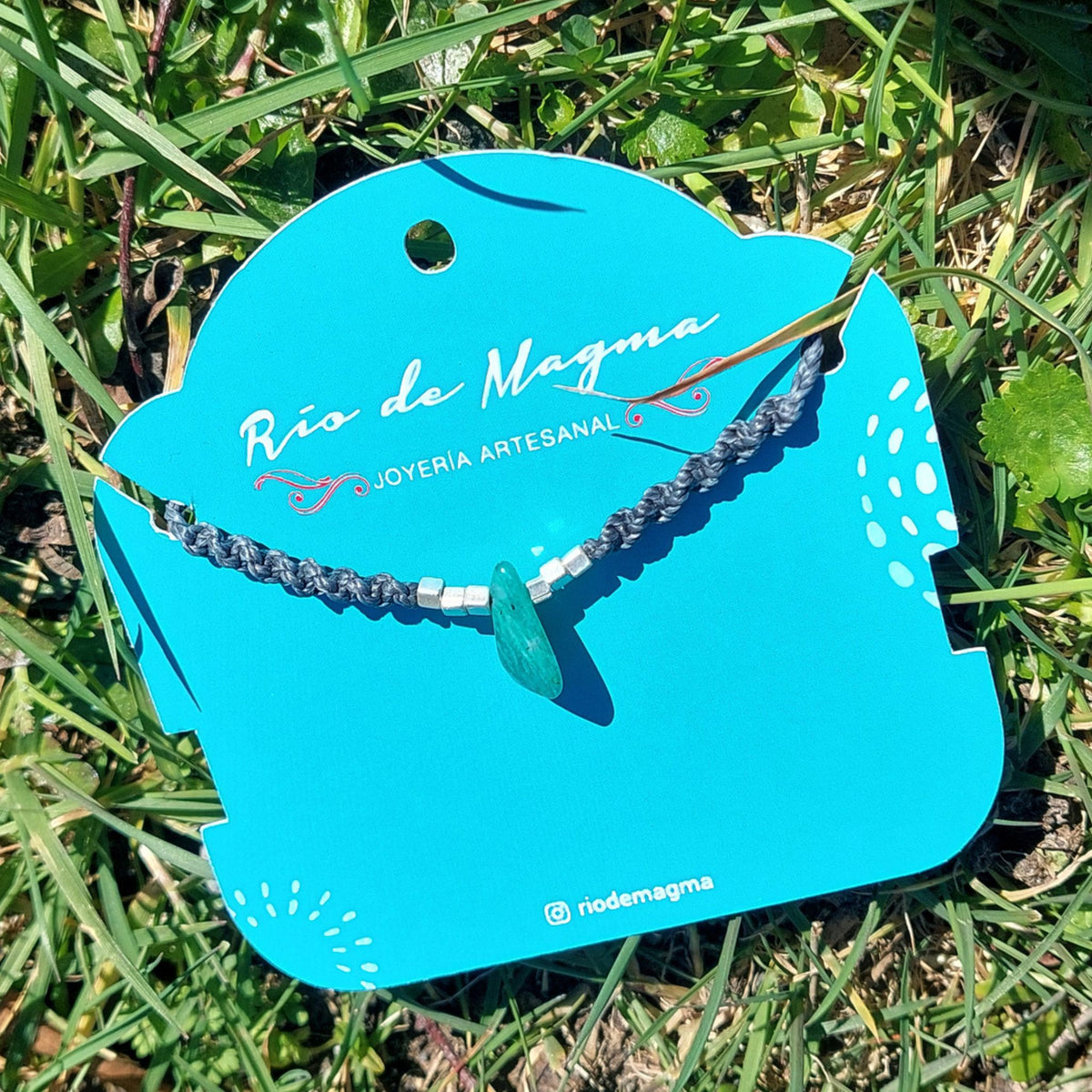 Vista lateral del Collar Luz de amazonita natural en macramé gris con cuentas de plata 950, destacando la forma irregular y color verde turquesa de la piedra sobre tarjeta de Río de Magma