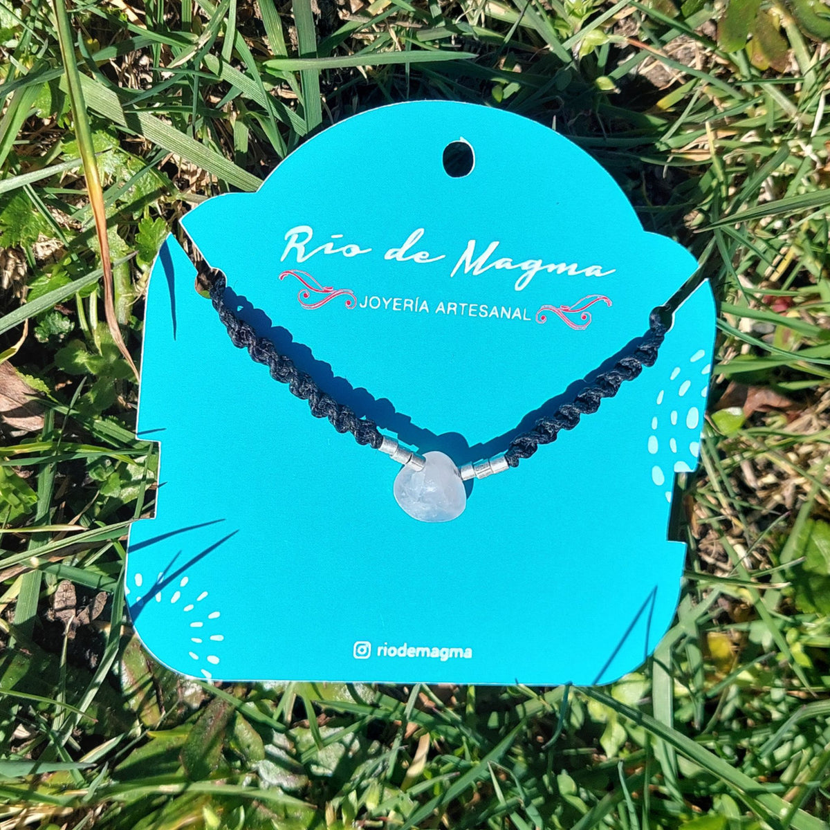 Vista frontal del Collar Luz de cuarzo rosa natural talla corazón en macramé negro con plata 950, mostrando la delicadeza y transparencia rosada de la piedra, sobre tarjeta de Río de Magma