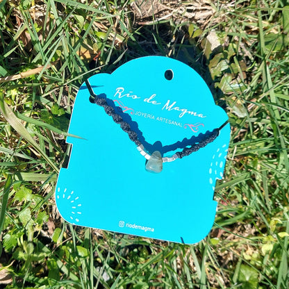 Collar Luz de prehnita natural en macramé negro con plata 950 sobre tarjeta de Río de Magma, vista en ángulo sobre fondo natural de pasto