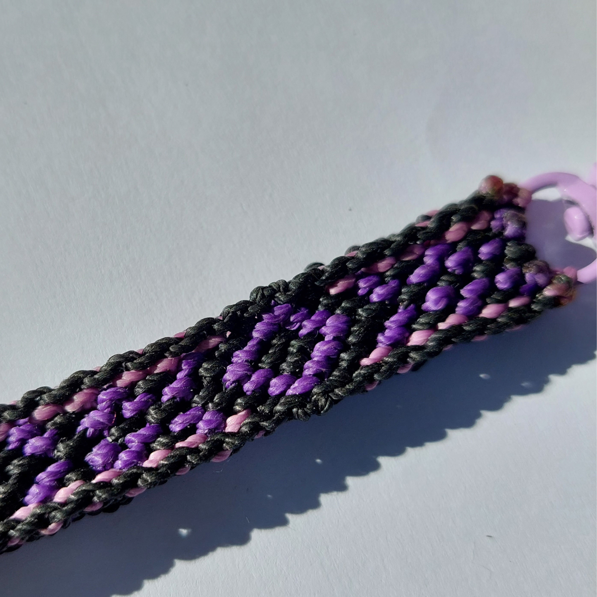 Detalle del tejido de macramé morado y negro con patrón geométrico para correa de celular.