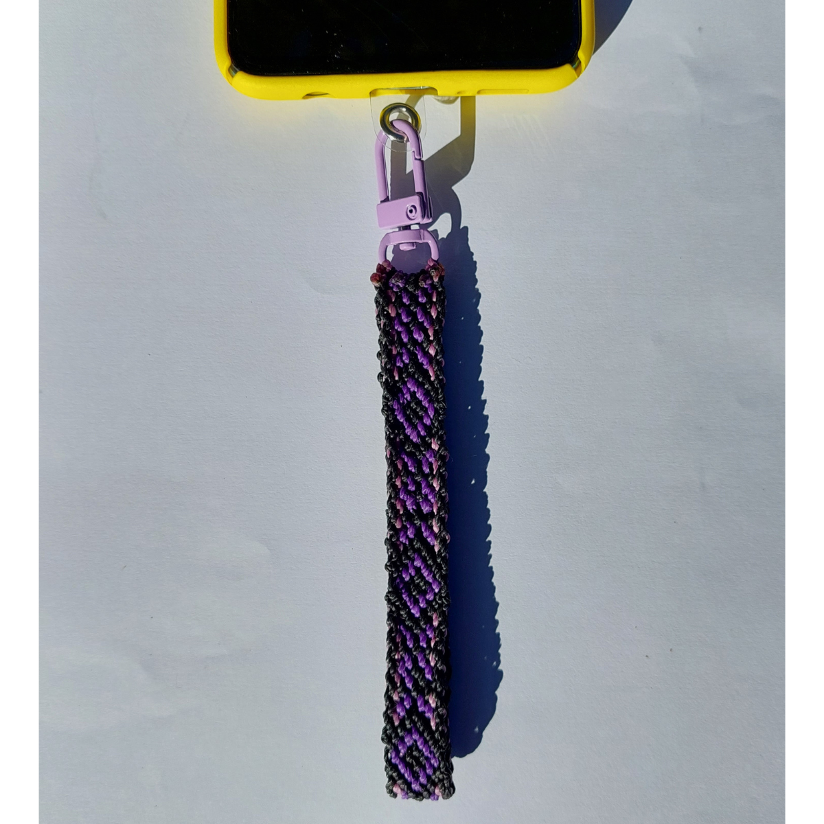 Correa de macramé morado y negro instalada en un celular, con diseño tejido a mano.