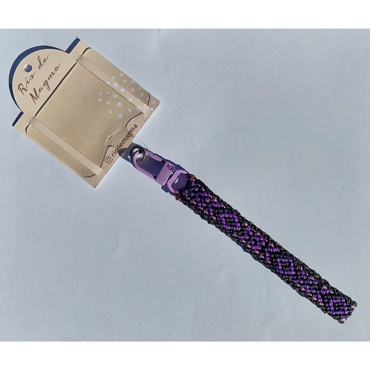 Correa para celular de macramé morado y negro conectada a un adaptador universal de carcasa.