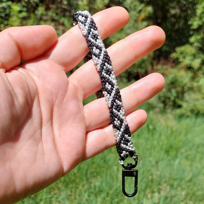 Pulsera para celular de macramé gris con diseño geométrico, mostrada sobre la palma de la mano.