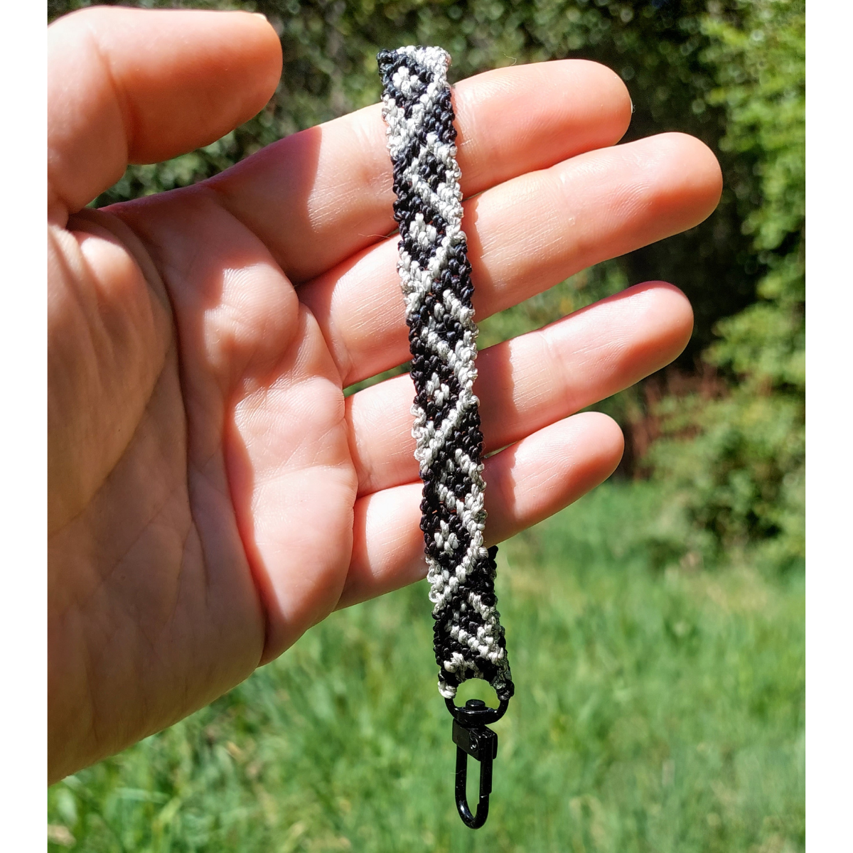 Correa de macramé negro y plateado con patrón geométrico para llevar el celular en la muñeca.