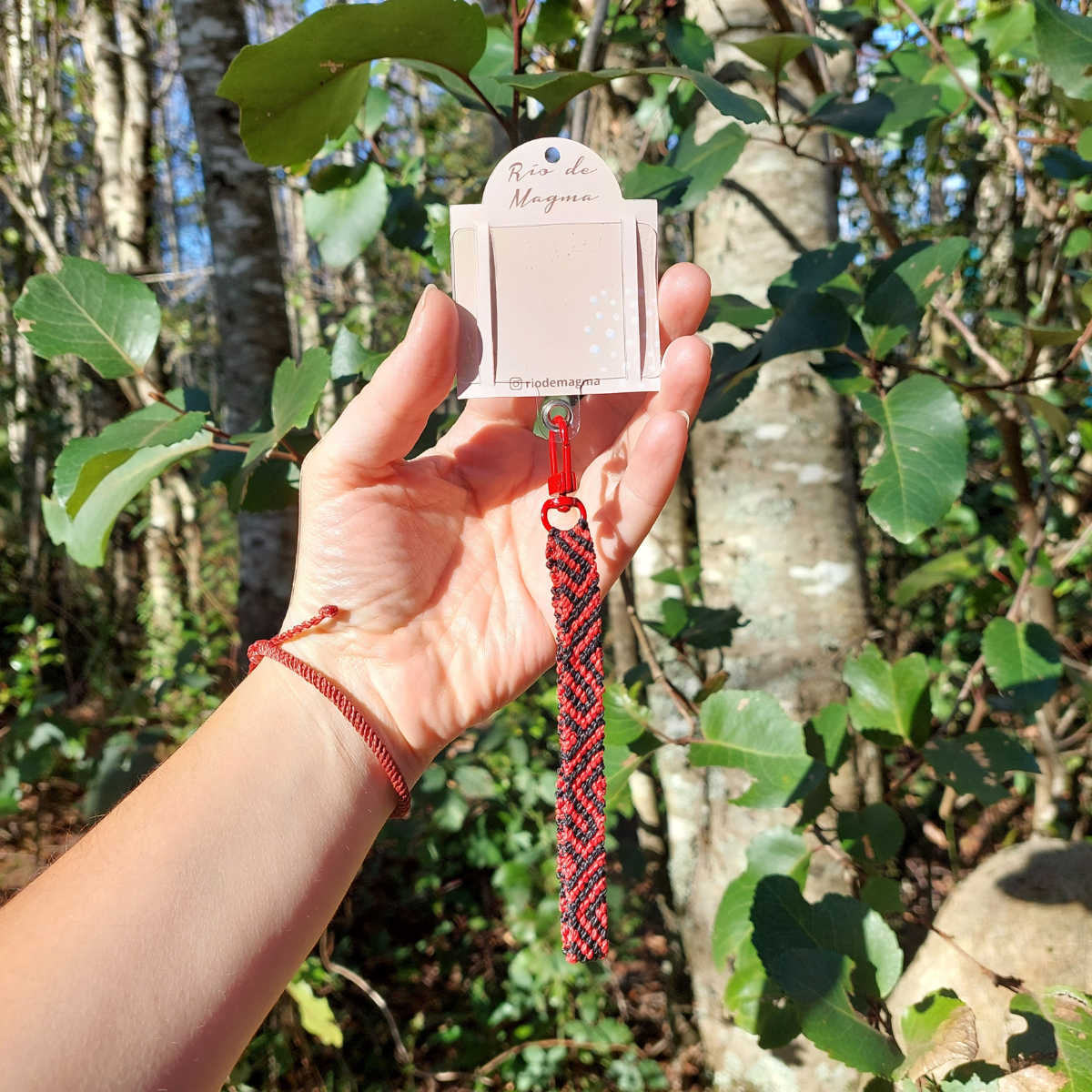 Correa artesanal de macramé roja conectada a la carcasa de un celular mediante adaptador.
