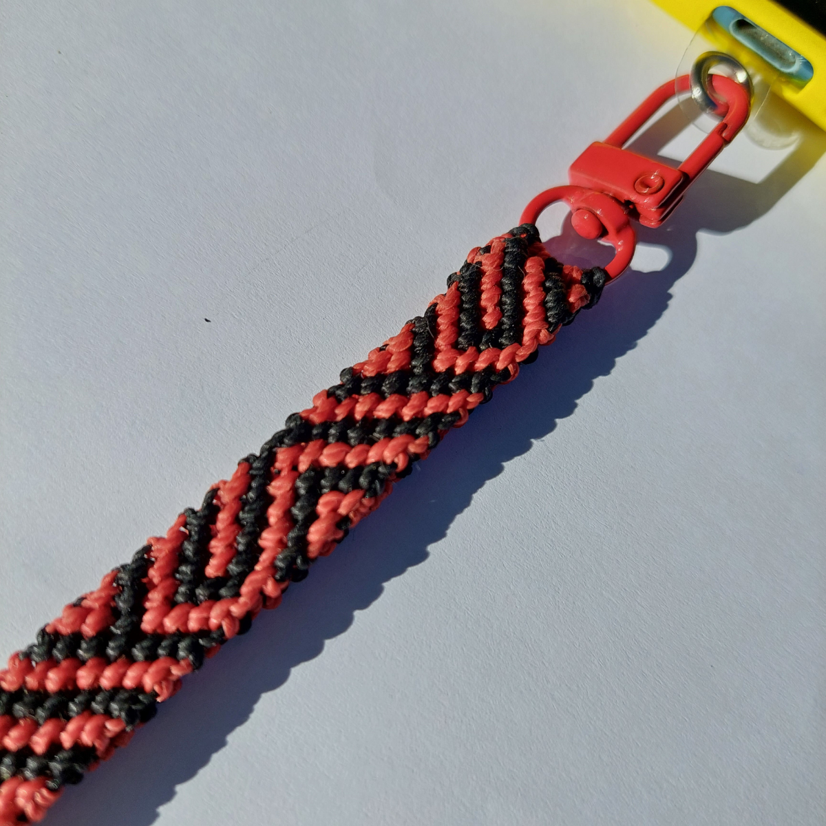 Correa para celular de macramé rojo y negro con diseño geométrico y mosquetón, hecha a mano en Pucón.