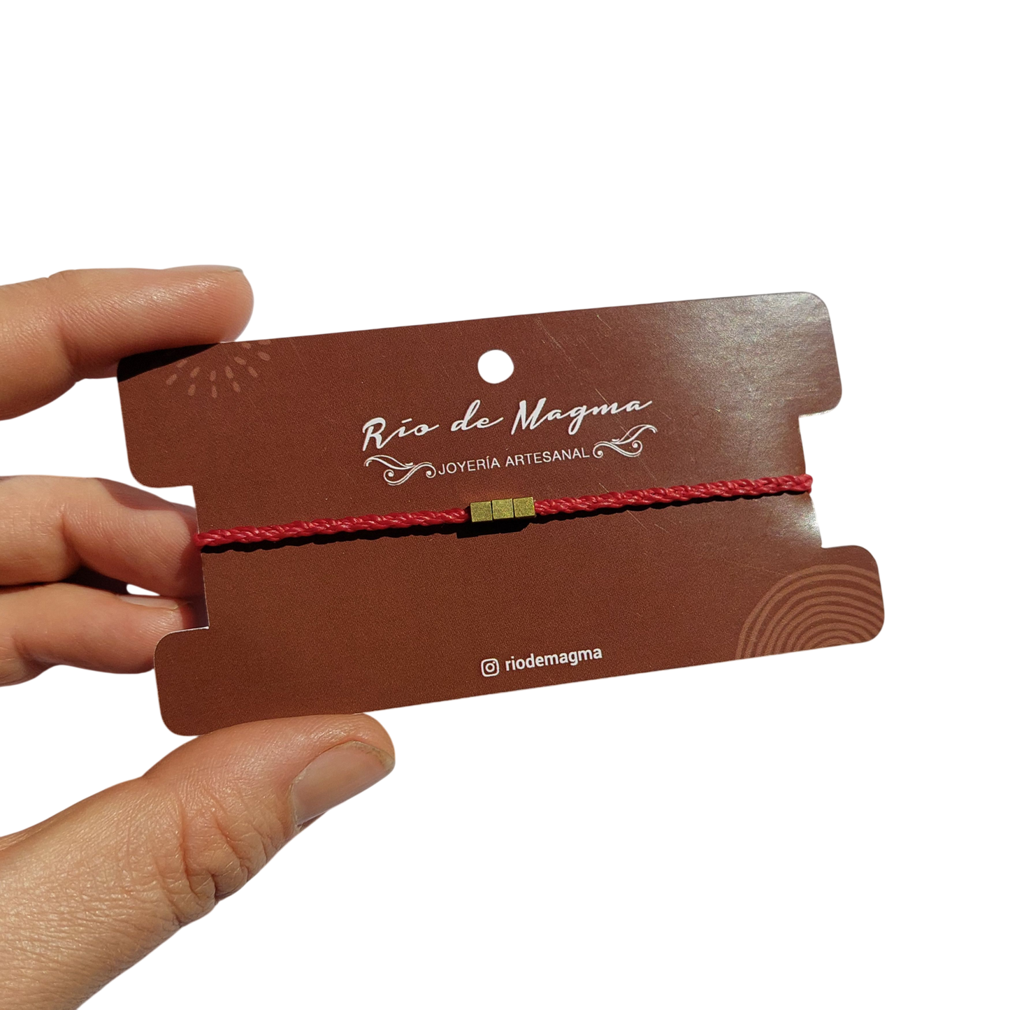 Pulsera minimalista con cuentas de bronce en hilo rojo, montada en tarjeta Río de Magma, fondo blanco
