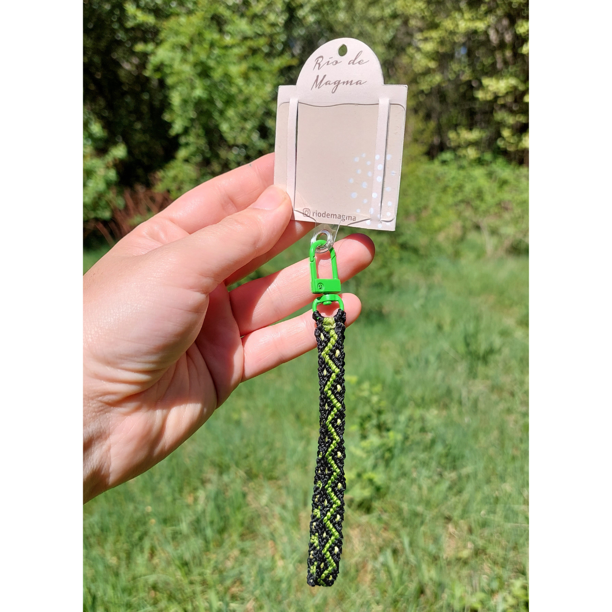 Detalle del adaptador universal con correa de macramé verde y enganche metálico para celular.